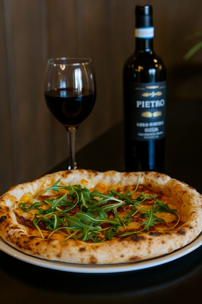 Pizza con rúcula fresca y tomate, acompañada de una copa de vino tinto